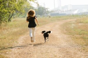 A woman jogging with her dog along a sunny path in a park, showcasing outdoor fitness and companionship.